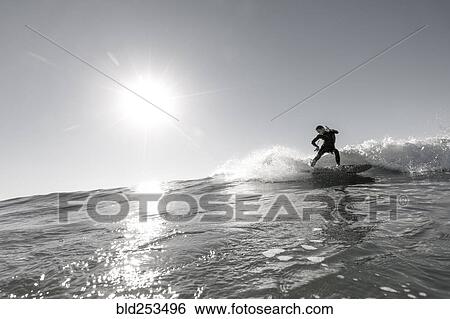 Stock Photograph - Distant Caucasian man surfing in sunny ocean. Fotosearch