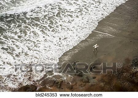 Stock Image - Distant Caucasian woman throwing stone on ocean beach. Fotosearch