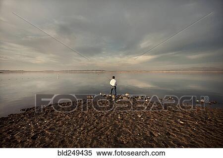 Stock Photography - Distant man fishing on beach. Fotosearch