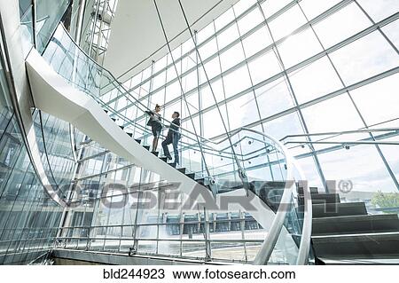 Stock Image - Distant Mixed Race business people standing on staircase and talking. Fotosearch