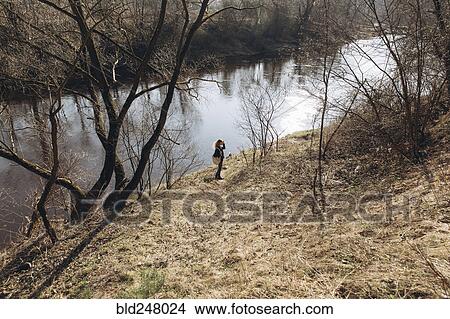 Picture - Distant woman standing near river. Fotosearch