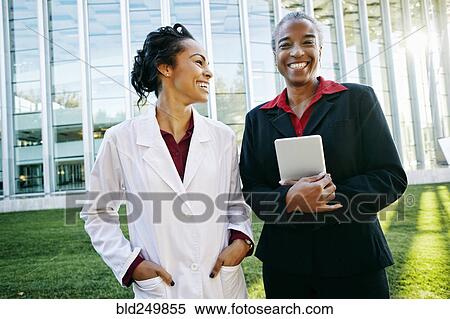 Stock Photography - Doctor and administrator laughing outdoors at hospital. Fotosearch