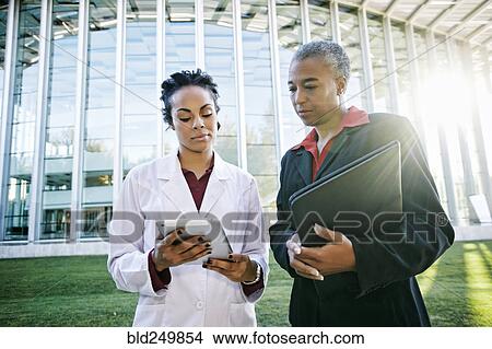 Doctor and administrator outdoors at hospital using digital tablet View Large Photo Image Picture - Doctor and administrator outdoors at hospital using digital tablet. Fotosearch