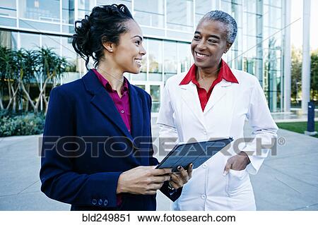 Stock Image - Doctor and administrator outdoors at hospital using digital tablet. Fotosearch