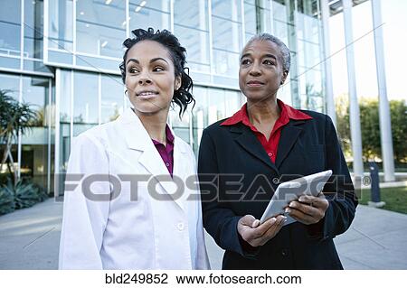 Stock Image - Doctor and administrator outdoors at hospital using digital tablet. Fotosearch