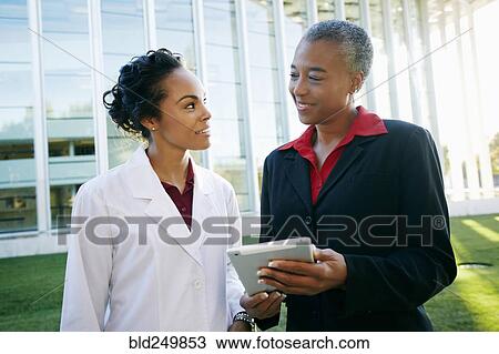 Stock Image - Doctor and administrator outdoors at hospital using digital tablet. Fotosearch