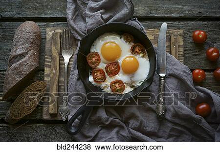 Stock Photo - Eggs and tomatoes in frying pan on wooden table. Fotosearch