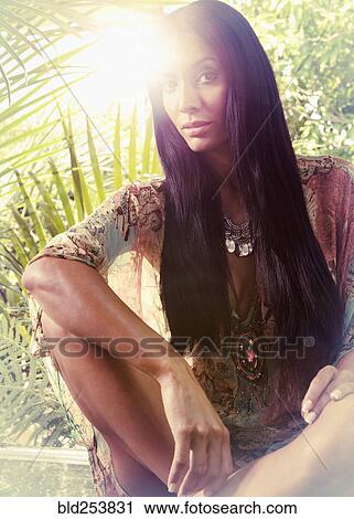 Stock Image - Exotic Hispanic woman sitting near foliage. Fotosearch