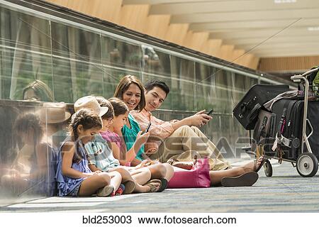 Family waiting on floor of airport using cell phones View Large Photo Image Stock Image - Family waiting on floor of airport using cell phones. Fotosearch