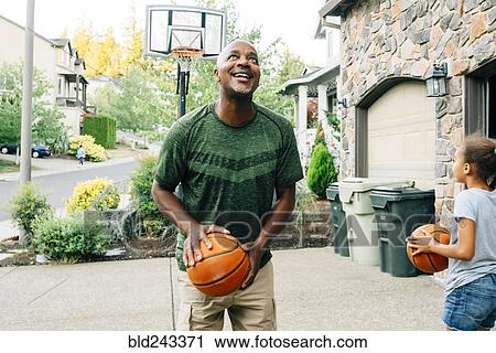 Stock Image - Father and daughter playing basketball in driveway. Fotosearch