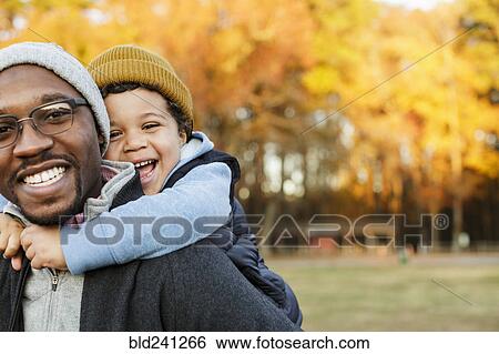Stock Photograph - Father carrying son piggyback in park. Fotosearch