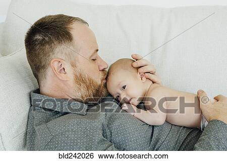 Stock Photograph - Father laying on sofa kissing baby daughter on head. Fotosearch