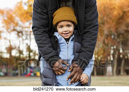Stock Image - Father leaning over son in park. Fotosearch