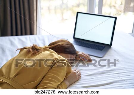 Stock Photo - Fatigued Caucasian woman sleeping on bed near laptop. Fotosearch