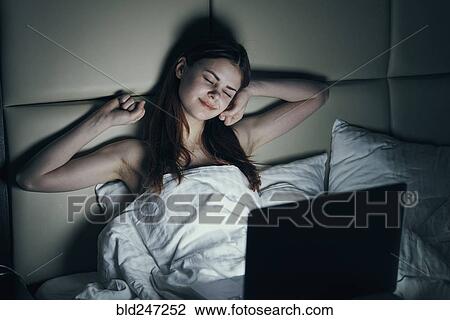 Stock Image - Fatigued Caucasian woman using laptop in bed. Fotosearch