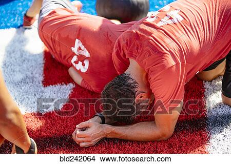 Picture - Fatigued men resting on artificial turf field. Fotosearch