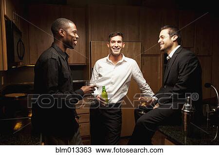 Stock Image - Friends drinking in kitchen at party. Fotosearch