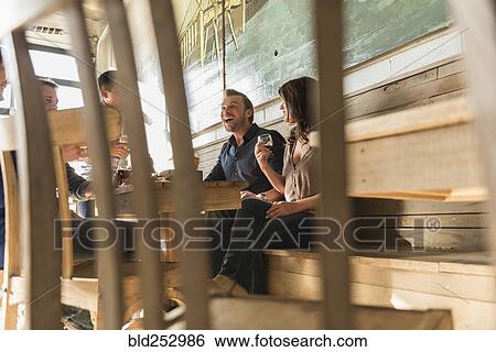 Stock Photograph - Friends laughing in brew pub behind chair. Fotosearch