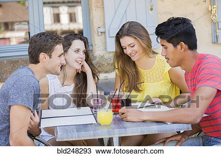 Stock Image - Friends reading menus at restaurant. Fotosearch