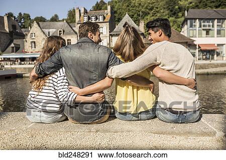 Stock Image - Friends sitting and hugging at waterfront. Fotosearch