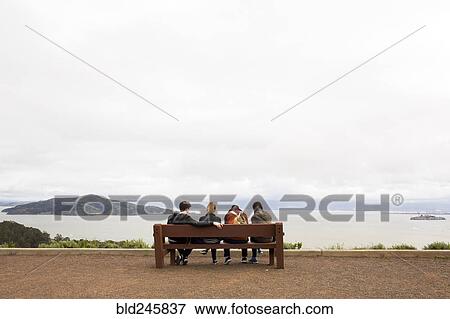 Friends sitting on bench admiring scenic view of ocean View Large Photo Image Stock Photo - Friends sitting on bench admiring scenic view of ocean. Fotosearch