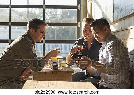 Stock Image - Friends texting on cell phone in brew pub. Fotosearch