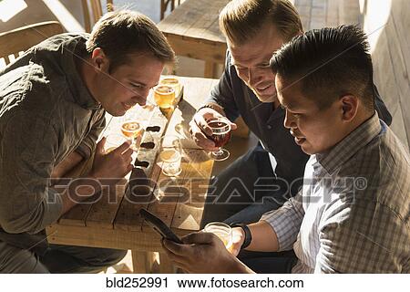 Stock Image - Friends texting on cell phone in brew pub. Fotosearch