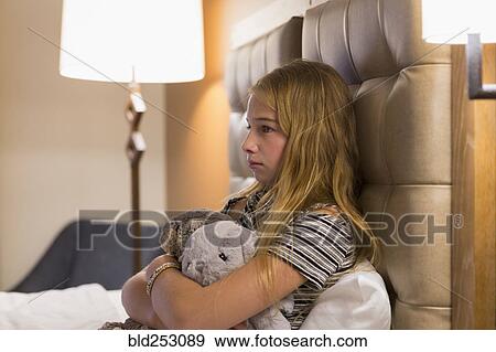 Stock Photo - Frustrated Caucasian girl holding stuffed animals on hotel bed. Fotosearch