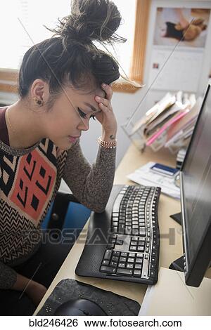 Stock Photograph - Frustrated Mixed Race woman sitting at desk using computer. Fotosearch
