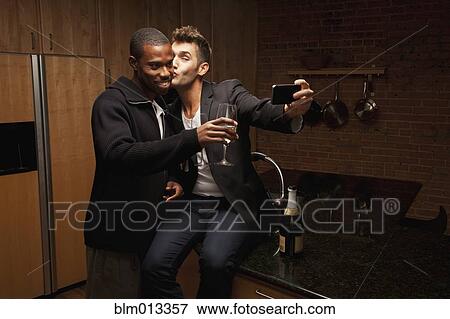 Gay couple drinking wine in kitchen and taking self-portraits View Large Photo Image Stock Photo - Gay couple drinking wine in kitchen and taking self-portraits. Fotosearch