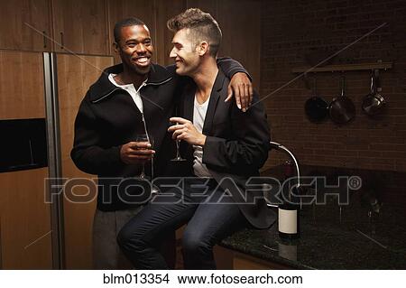 Picture - Gay couple drinking wine in kitchen. Fotosearch