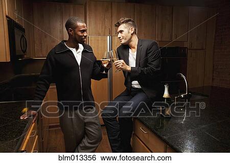 Stock Photograph - Gay couple drinking wine in kitchen. Fotosearch