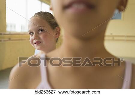 Stock Photo - Girl peeking over shoulder of girl in ballet studio. Fotosearch