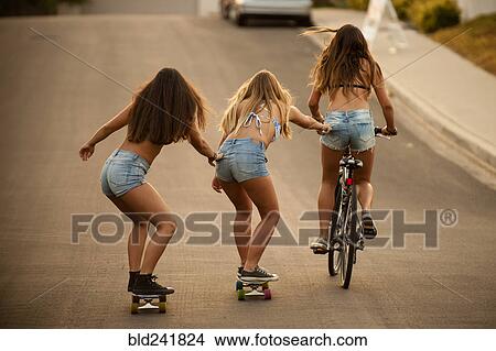 Picture - Girl riding bicycle pulling friends on skateboard. Fotosearch