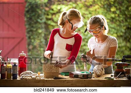 Stock Photo - Girls examining thumb while building birdhouse in garage. Fotosearch