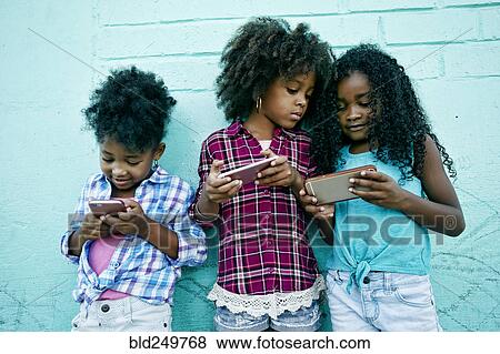 Girls leaning on wall texting on cell phones View Large Photo Image Stock Photo - Girls leaning on wall texting on cell phones. Fotosearch