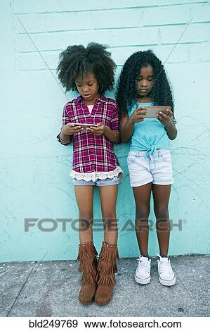 Girls leaning on wall texting on cell phones View Large Photo Image Stock Photo - Girls leaning on wall texting on cell phones. Fotosearch
