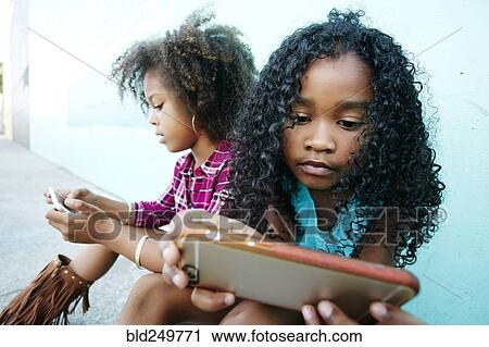 Girls sitting on sidewalk texting on cell phones View Large Photo Image Stock Image - Girls sitting on sidewalk texting on cell phones. Fotosearch