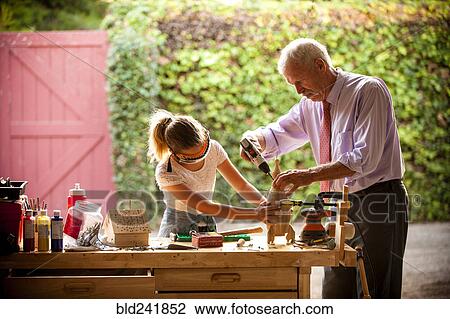 Stock Image - Grandfather and granddaughter building birdhouse in garage. Fotosearch