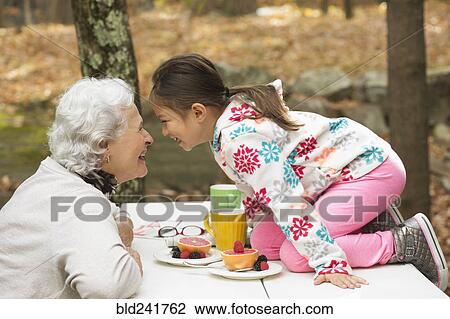 Stock Image - Grandmother and granddaughter playing at breakfast table outdoors. Fotosearch