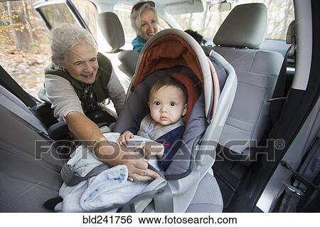 Grandmother fastening baby grandson in car seat View Large Photo Image Stock Photograph - Grandmother fastening baby grandson in car seat. Fotosearch