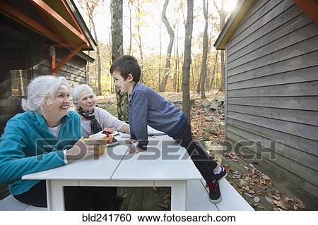 Stock Image - Grandmothers enjoying breakfast outdoors near cabin with grandson. Fotosearch