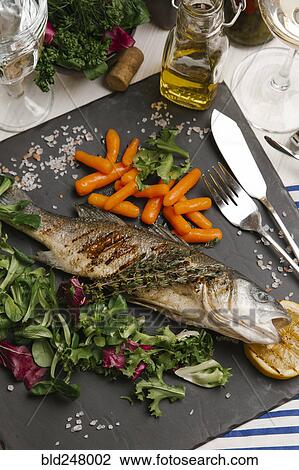 Stock Image - Grilled fish and salad on stone plate. Fotosearch