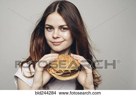 Picture - Grinning Caucasian woman holding cheeseburger. Fotosearch