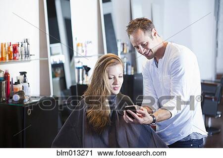 Stock Image - Hairdresser showing cell phone to client. Fotosearch