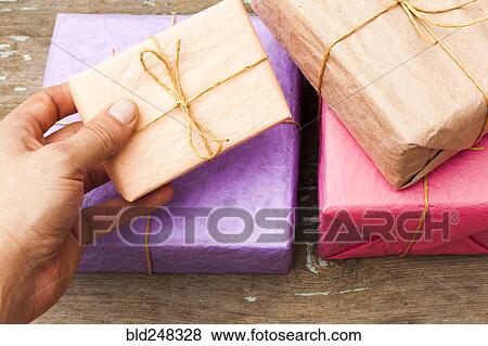Hand holding wrapped gifts on wooden table View Large Photo Image Stock Photo - Hand holding wrapped gifts on wooden table. Fotosearch