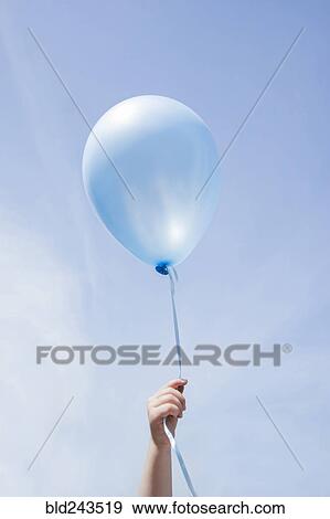 Stock Photo - Hand of Caucasian girl holding blue balloon in blue sky. Fotosearch
