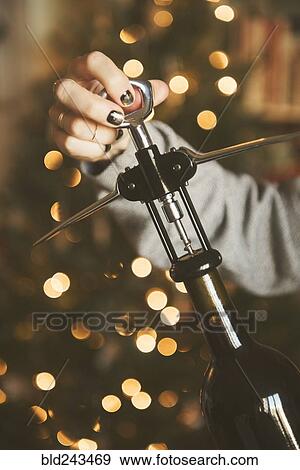 Stock Photo - Hand of Caucasian woman opening wine bottle with corkscrew. Fotosearch
