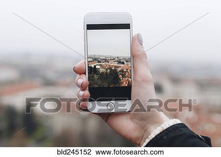Stock Image - Hand of Caucasian woman photographing cityscape with cell phone. Fotosearch