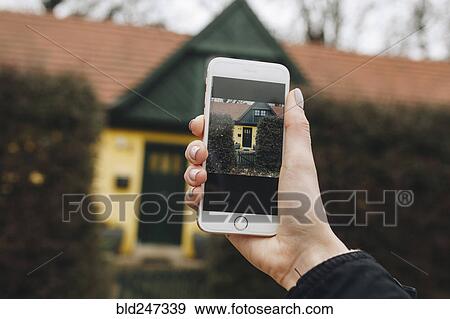 Stock Photo - Hand of Caucasian woman photographing house with cell phone. Fotosearch
